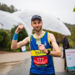 Runner stands in front of the Eden Project Biome fist pumping the air and holding his medal